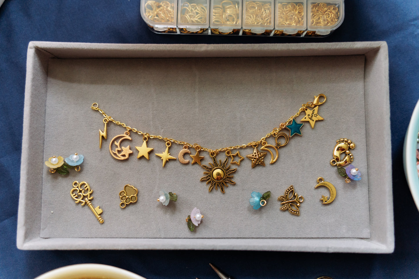 Gold charm bracelet with various charms on a gray tray