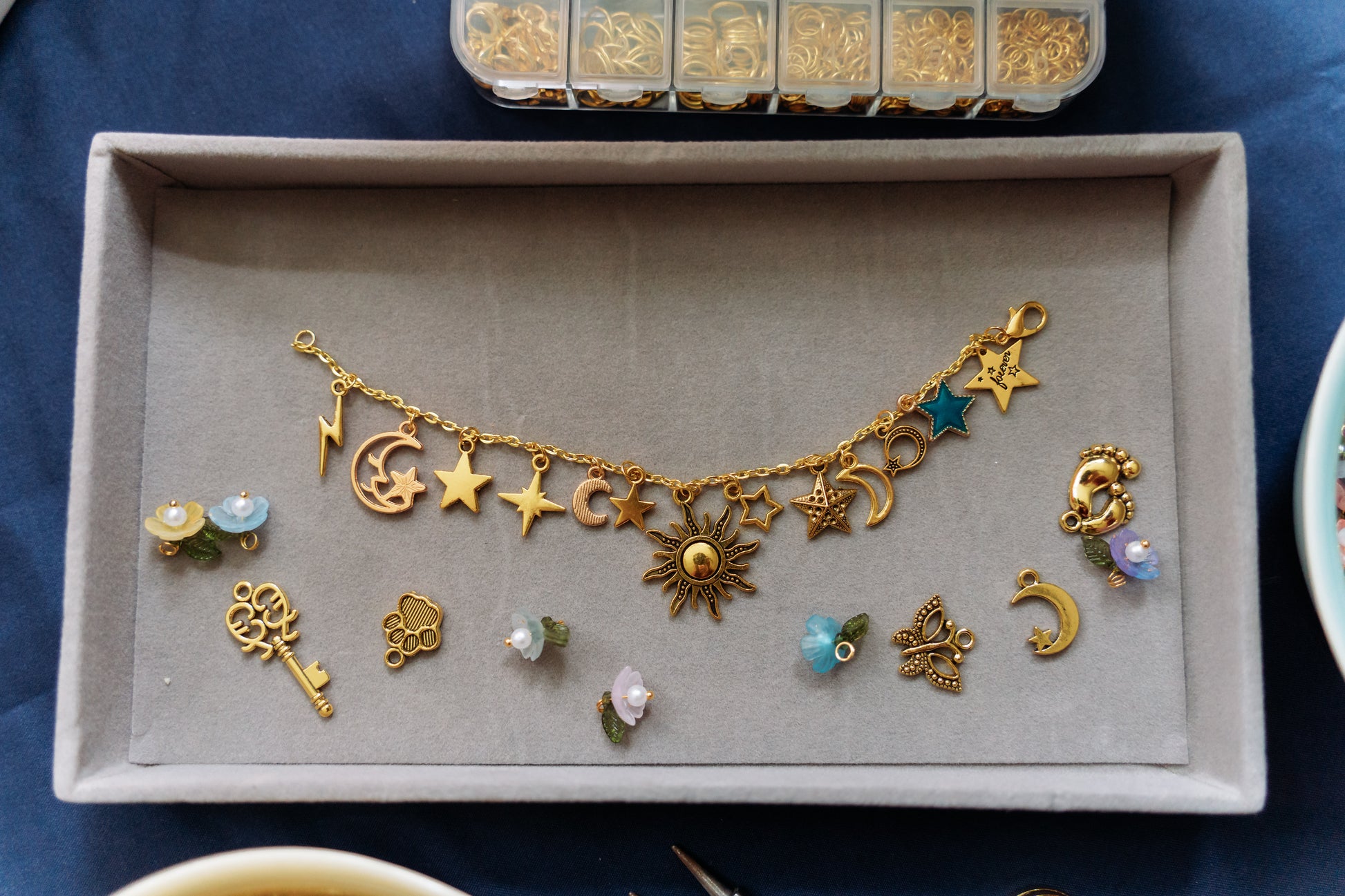 Gold charm bracelet with various charms on a gray tray