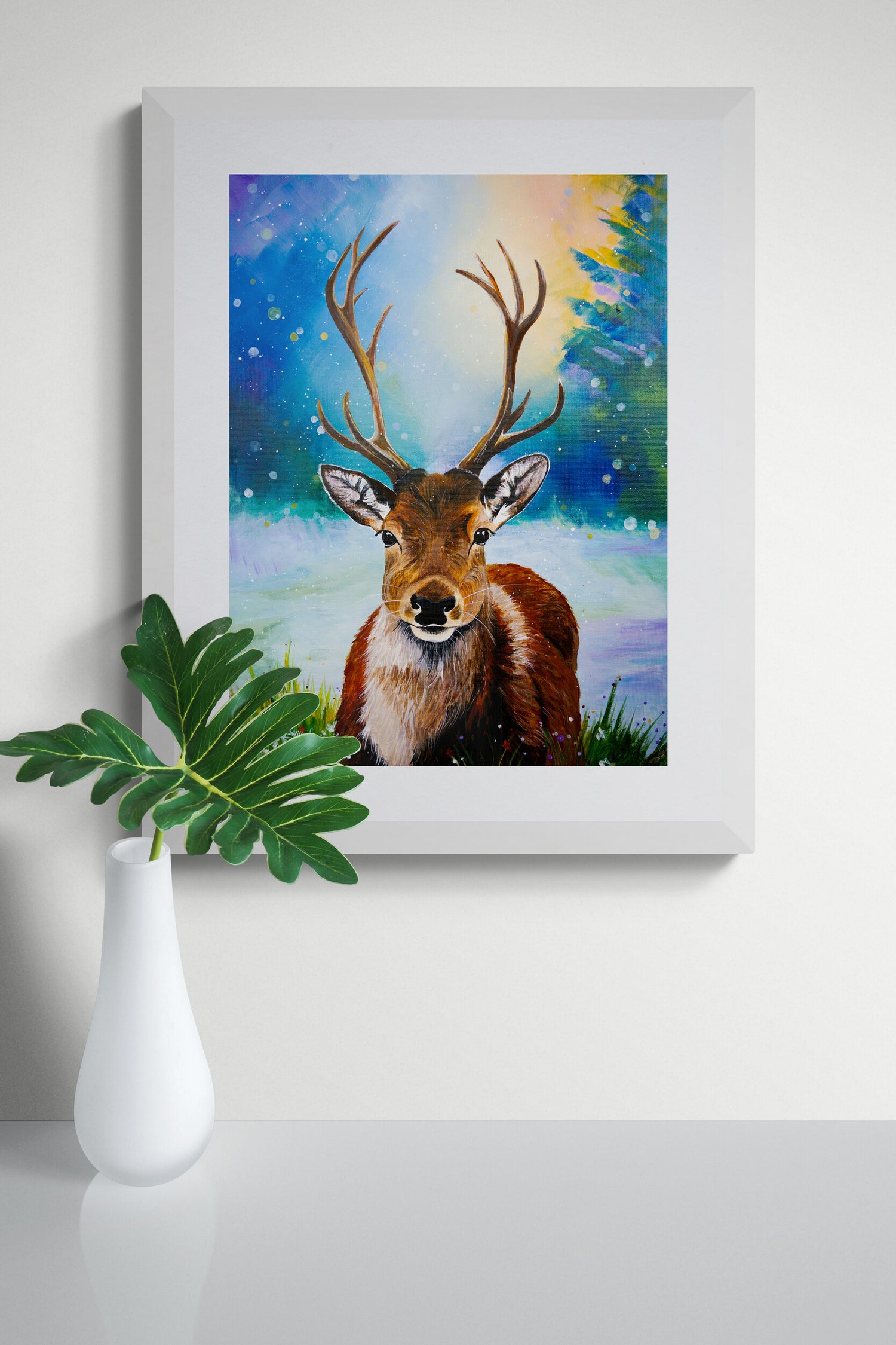 Framed artwork of a deer with a starry night background on a white surface with a plant.